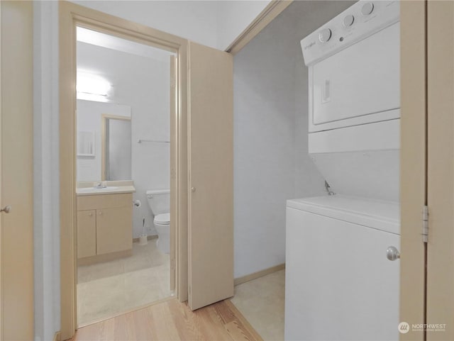 clothes washing area featuring stacked washing maching and dryer, sink, and light wood-type flooring