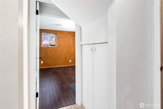 hallway featuring baseboards, hardwood / wood-style flooring, and wooden walls