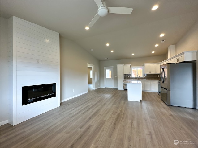 kitchen with a kitchen island, vaulted ceiling, white cabinetry, light wood-type flooring, and appliances with stainless steel finishes