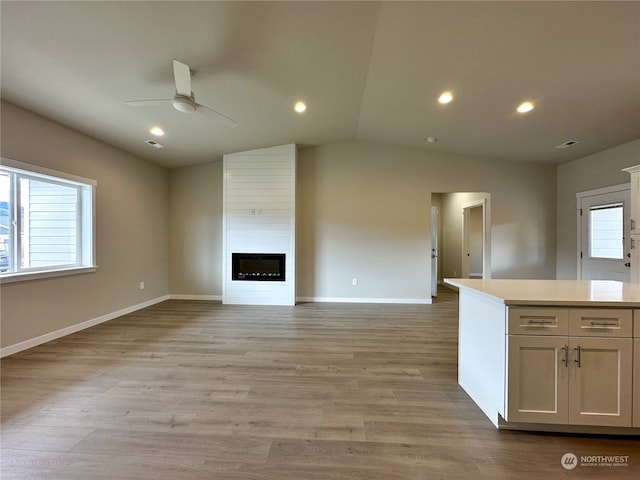 unfurnished living room featuring light hardwood / wood-style floors, lofted ceiling, a fireplace, and ceiling fan