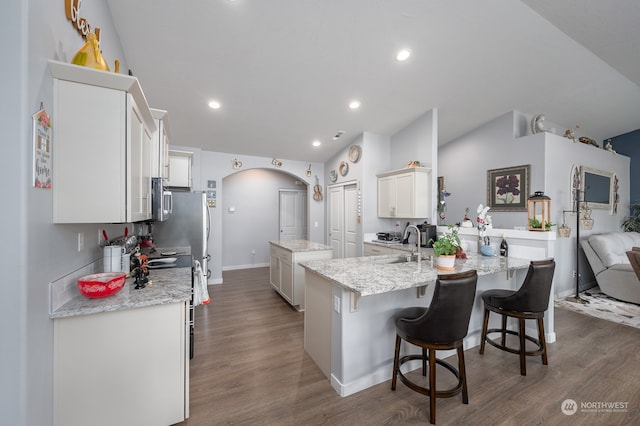 kitchen featuring white cabinetry, stainless steel appliances, dark wood-type flooring, light stone counters, and a center island with sink