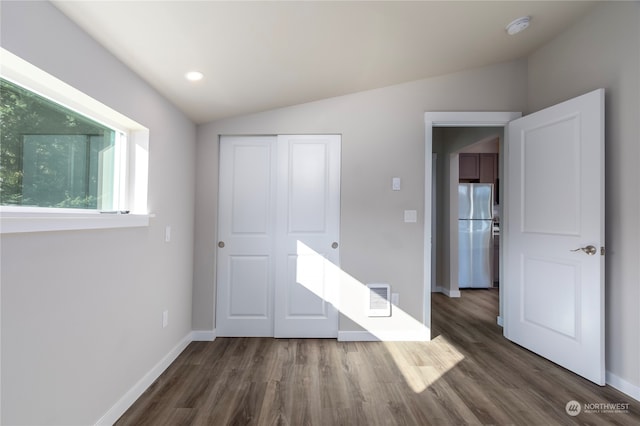 unfurnished bedroom with dark wood-type flooring, a closet, stainless steel refrigerator, and lofted ceiling