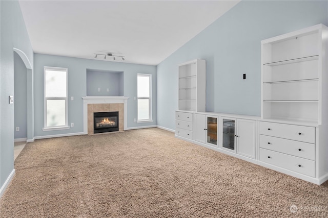 unfurnished living room with light carpet, built in features, vaulted ceiling, and a fireplace