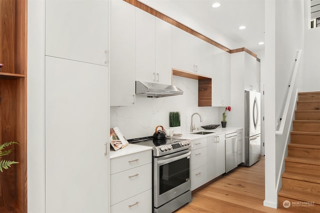 kitchen featuring appliances with stainless steel finishes, light wood-type flooring, tasteful backsplash, sink, and white cabinetry