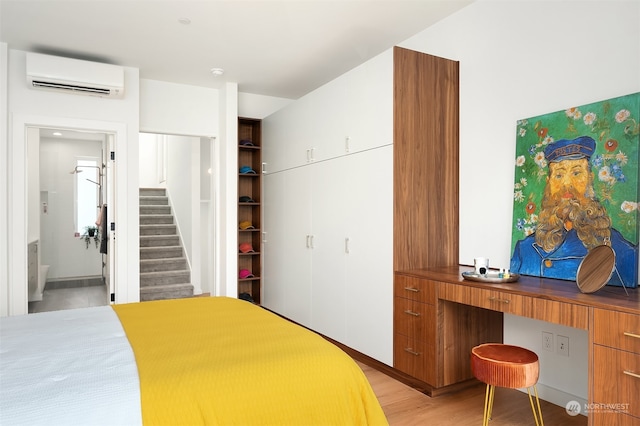 bedroom featuring a wall unit AC, connected bathroom, and light hardwood / wood-style floors