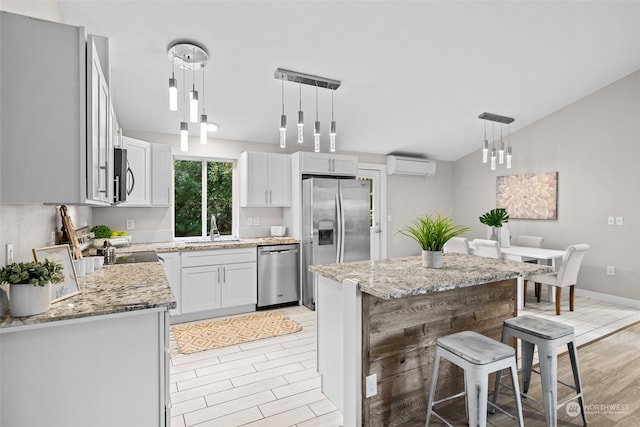 kitchen with sink, appliances with stainless steel finishes, a wall mounted air conditioner, hanging light fixtures, and a kitchen island