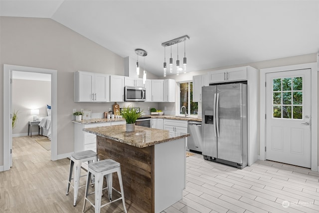 kitchen with stainless steel appliances, white cabinetry, decorative light fixtures, a center island, and light wood-type flooring