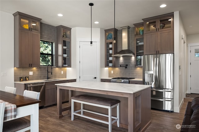 kitchen featuring wall chimney range hood, hanging light fixtures, dark hardwood / wood-style flooring, stainless steel appliances, and a center island