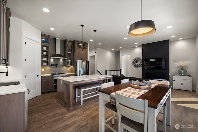 kitchen featuring appliances with stainless steel finishes, a center island, hanging light fixtures, wall chimney exhaust hood, and dark hardwood / wood-style floors