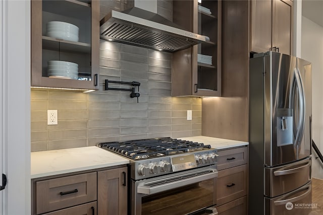 kitchen with wall chimney exhaust hood, decorative backsplash, stainless steel appliances, and light stone counters