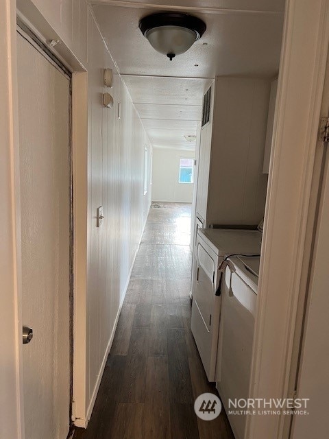 hallway with washing machine and clothes dryer, dark hardwood / wood-style floors, and wood walls