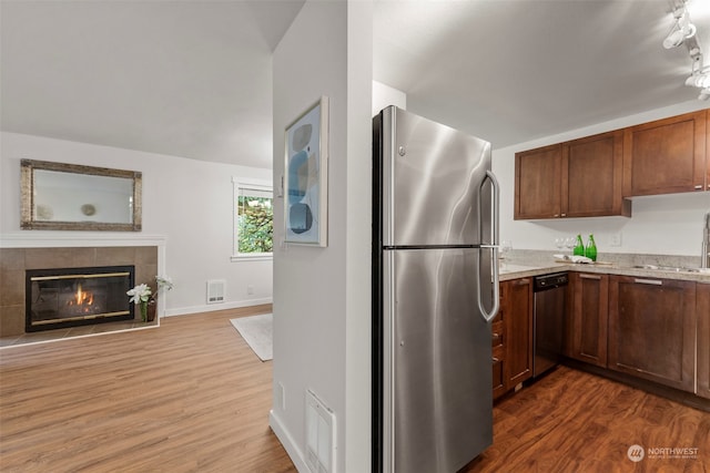 kitchen with a tiled fireplace, stainless steel appliances, light stone countertops, and dark hardwood / wood-style flooring