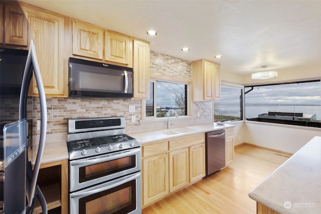 kitchen with appliances with stainless steel finishes, light brown cabinetry, tasteful backsplash, sink, and light hardwood / wood-style floors