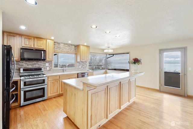 kitchen featuring light brown cabinets, black appliances, sink, light hardwood / wood-style flooring, and a kitchen island