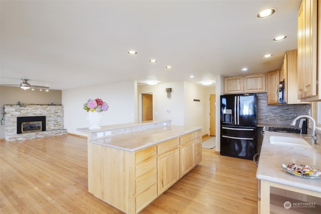 kitchen featuring black fridge, sink, a fireplace, light brown cabinetry, and light hardwood / wood-style floors