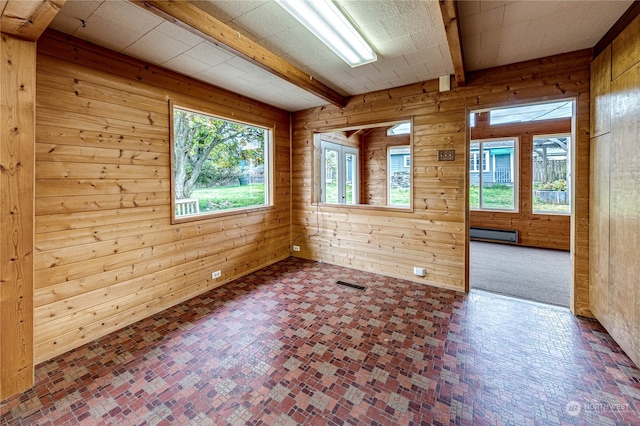 empty room with wood walls, a healthy amount of sunlight, and a baseboard radiator