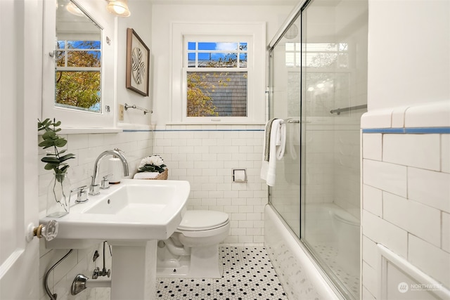 bathroom featuring tile walls, bath / shower combo with glass door, toilet, and tile patterned flooring