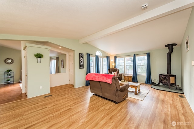 living room featuring a wood stove, light hardwood / wood-style flooring, and vaulted ceiling with beams