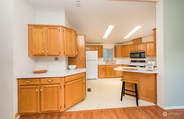 kitchen with white appliances, light hardwood / wood-style floors, and a breakfast bar