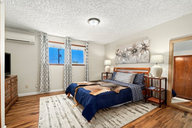 bedroom featuring hardwood / wood-style floors, a wall mounted AC, and a textured ceiling