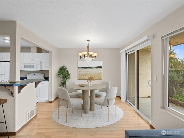 dining space featuring a textured ceiling, an inviting chandelier, and light wood-type flooring