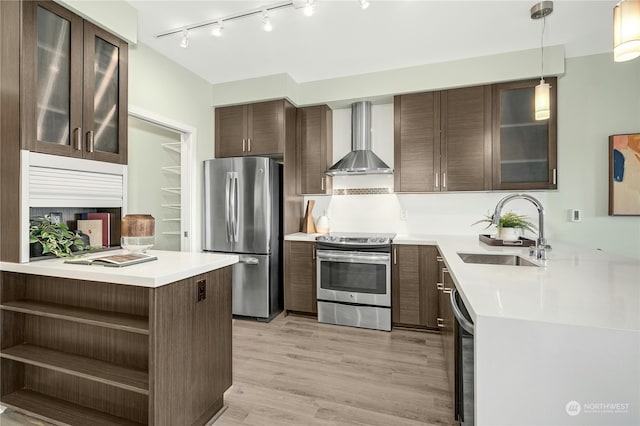 kitchen with wall chimney range hood, hanging light fixtures, kitchen peninsula, sink, and appliances with stainless steel finishes