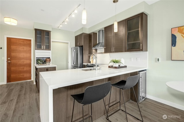 kitchen featuring hanging light fixtures, stainless steel refrigerator, dark hardwood / wood-style floors, wall chimney exhaust hood, and sink