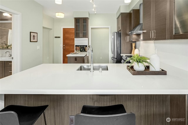 kitchen featuring a kitchen breakfast bar, wall chimney exhaust hood, sink, and stainless steel refrigerator