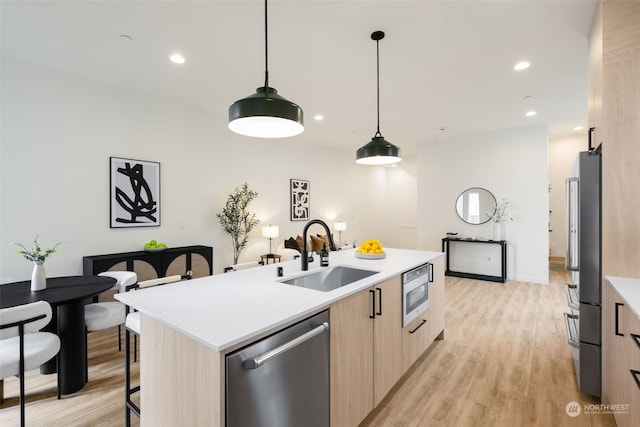 kitchen with appliances with stainless steel finishes, sink, light wood-type flooring, hanging light fixtures, and a center island with sink