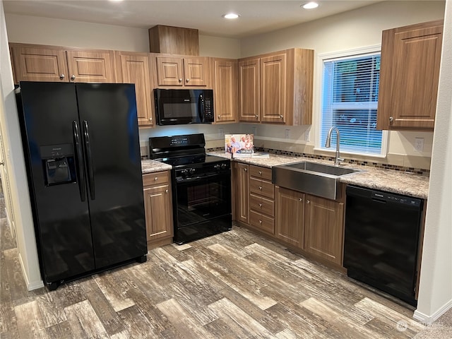 kitchen with light stone counters, black appliances, sink, and hardwood / wood-style floors