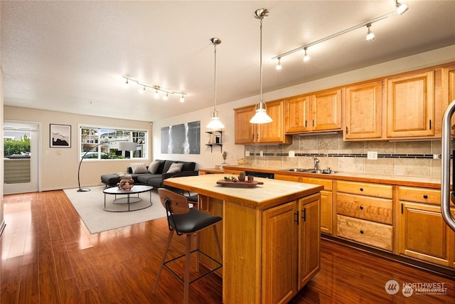 kitchen featuring sink, backsplash, a center island, dark hardwood / wood-style flooring, and hanging light fixtures