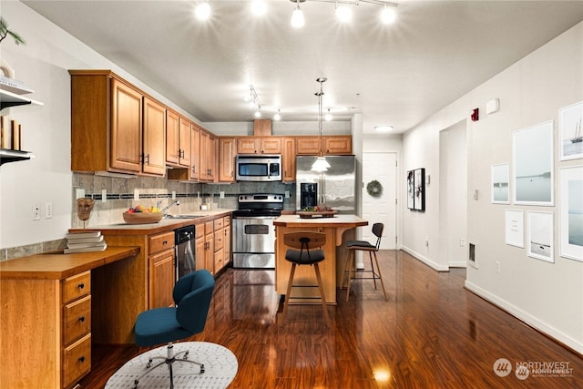 kitchen featuring decorative backsplash, a breakfast bar area, rail lighting, stainless steel appliances, and a center island