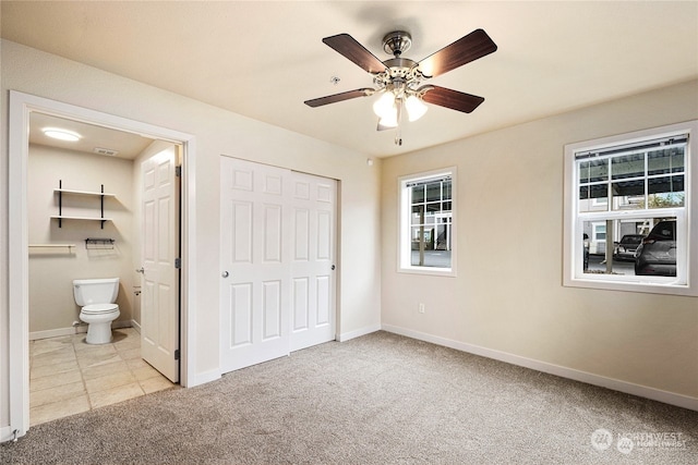 unfurnished bedroom with ensuite bath, a closet, light carpet, ceiling fan, and multiple windows