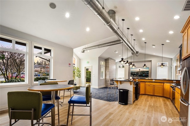 kitchen with a kitchen bar, kitchen peninsula, hanging light fixtures, light hardwood / wood-style floors, and lofted ceiling