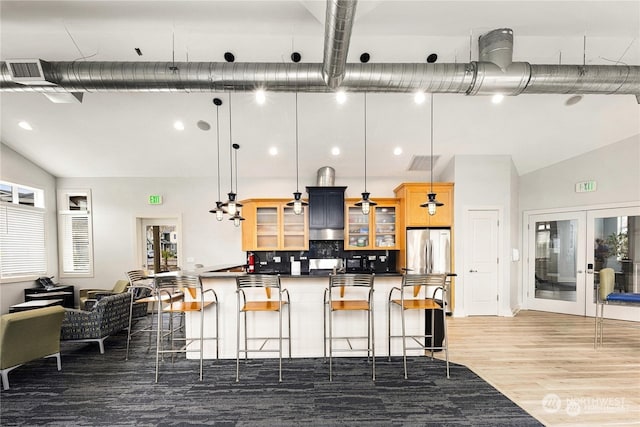 kitchen with stainless steel fridge, a kitchen breakfast bar, wood-type flooring, a wealth of natural light, and decorative light fixtures