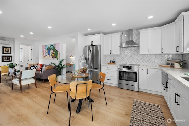 kitchen with white cabinets, wall chimney range hood, stainless steel appliances, and light hardwood / wood-style floors