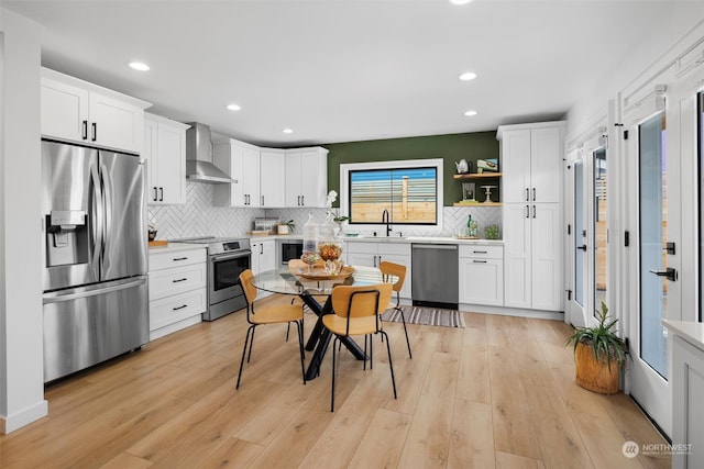 kitchen featuring white cabinets, wall chimney range hood, stainless steel appliances, and light hardwood / wood-style floors