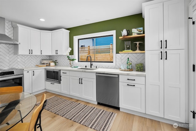 kitchen featuring wall chimney range hood, appliances with stainless steel finishes, sink, white cabinetry, and light hardwood / wood-style floors