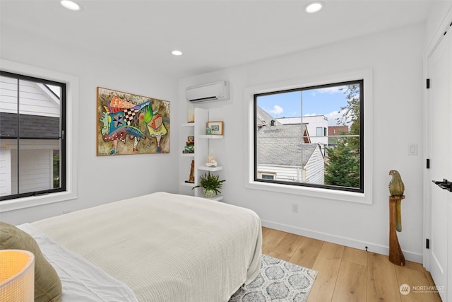 bedroom with a wall mounted AC, multiple windows, and light wood-type flooring