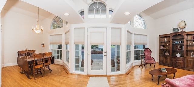 doorway with high vaulted ceiling, wood-type flooring, and an inviting chandelier