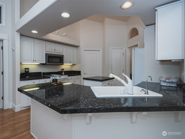 kitchen with kitchen peninsula, dark hardwood / wood-style flooring, white cabinetry, sink, and white appliances