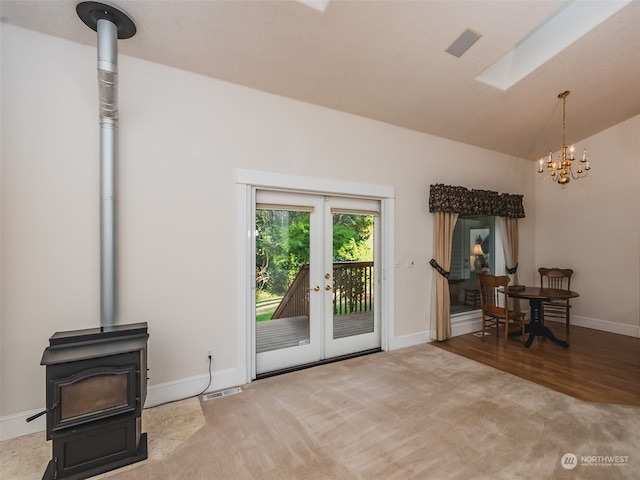 living room featuring french doors, a wood stove, hardwood / wood-style floors, lofted ceiling with skylight, and a notable chandelier