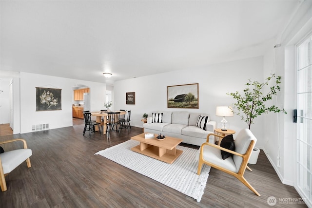 living area featuring baseboards, visible vents, arched walkways, and wood finished floors