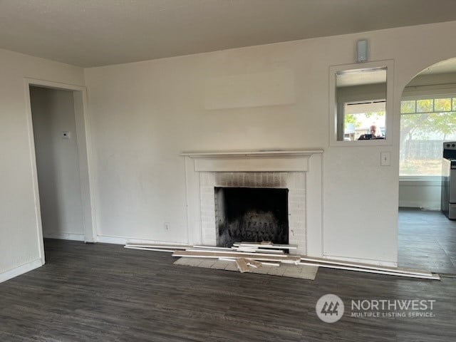 unfurnished living room featuring dark wood-type flooring and a brick fireplace