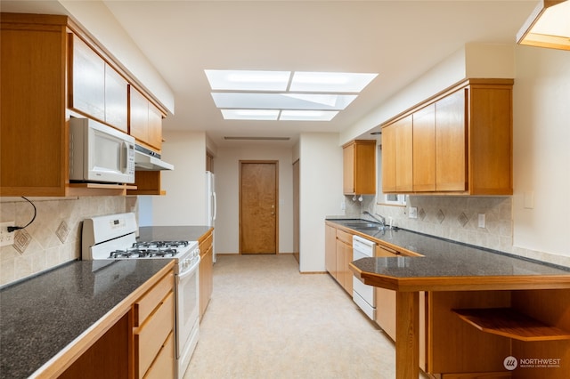 kitchen with white appliances, backsplash, a skylight, and sink