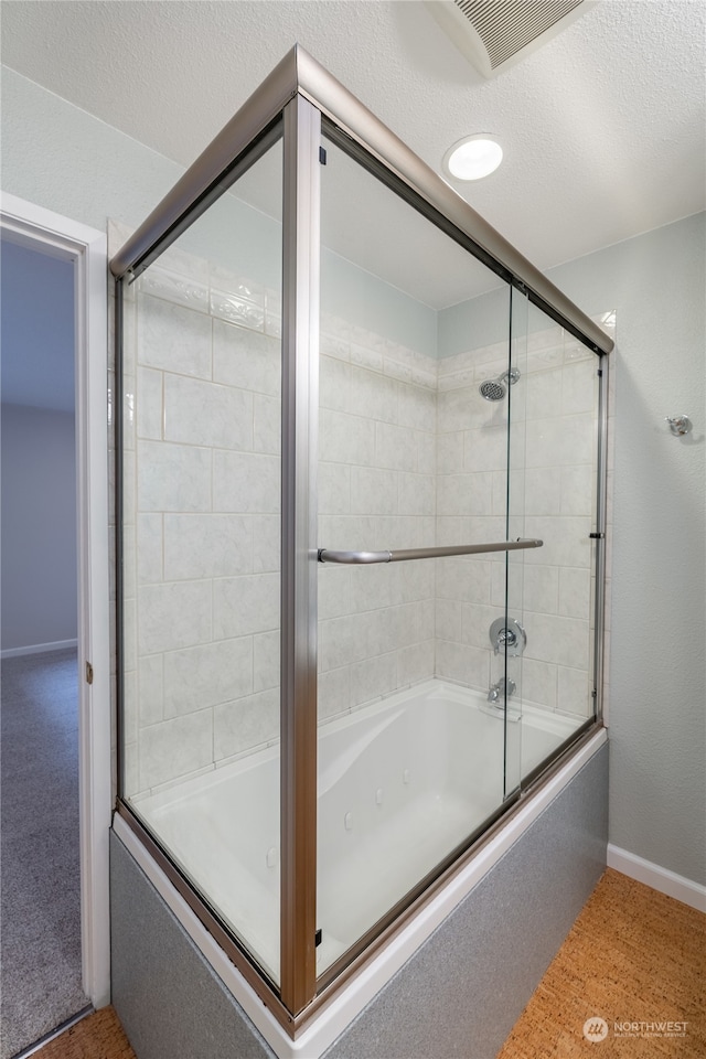 bathroom with a textured ceiling and shower / bath combination with glass door