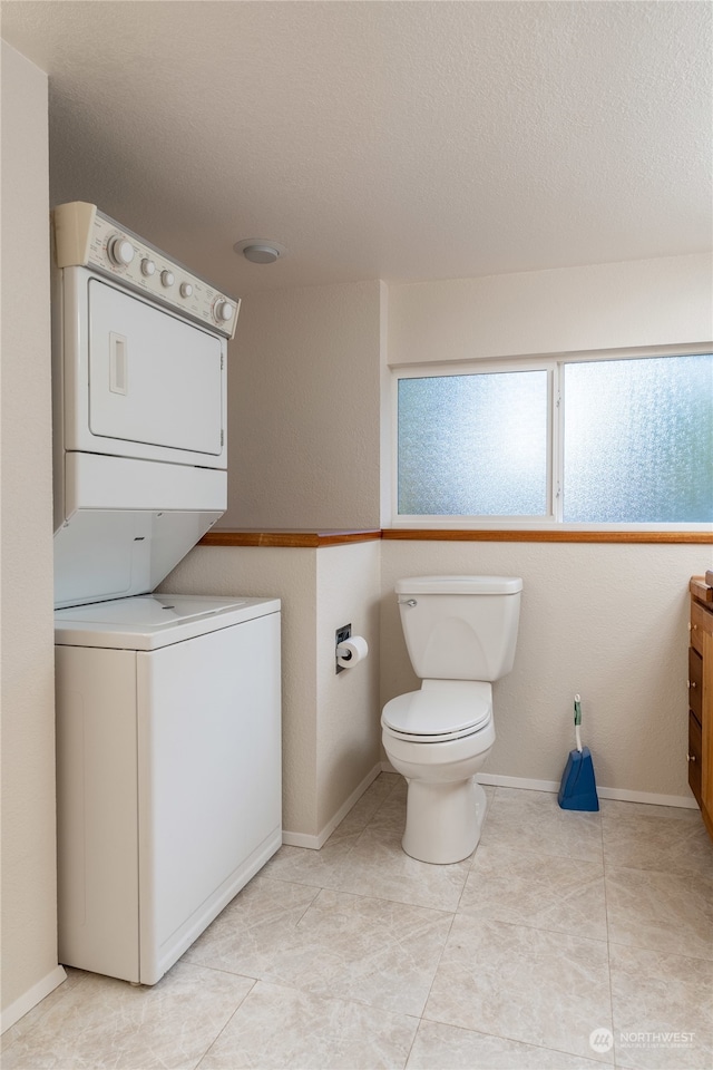 bathroom featuring toilet, a textured ceiling, stacked washer and dryer, and tile patterned flooring