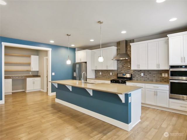 kitchen with wall chimney exhaust hood, white cabinets, stainless steel appliances, and light wood-type flooring