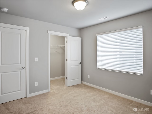 unfurnished bedroom with a walk in closet, a closet, and light colored carpet