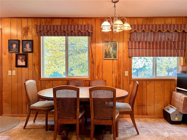 dining room featuring a notable chandelier, plenty of natural light, and wooden walls